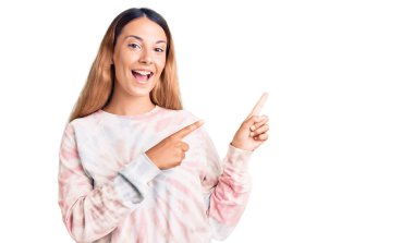 Güzel bir genç kadın, günlük kravat boyası kazak giyiyor gülümsüyor ve kameraya bakıyor. İki eli ve parmağı yana bakıyor.. 