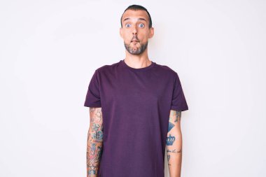 Dövmesi olan, sıradan kıyafetler giyen, dudaklarıyla balık suratı yapan, çılgın ve komik bir jest yapan yakışıklı bir genç. Komik ifade. 