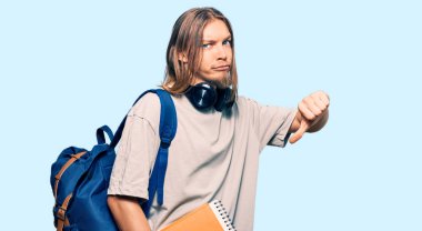 Uzun saçlı, yakışıklı, öğrenci çantası takan ve elinde kızgın yüzlü kitaplar tutan beyaz bir adam. Negatif işaretler, baş parmakları aşağıda, reddedilme kavramı. 