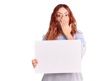 Elinde boş pankart tutan genç Latin kadın ağzını eliyle kapatıyor, şaşırmış ve hata yapmaktan korkuyor. şaşırmış ifade 