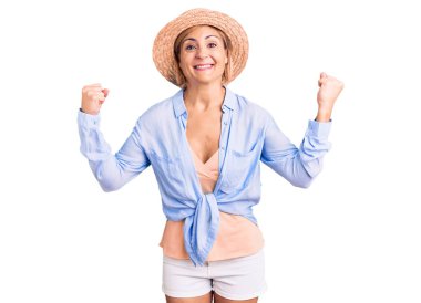 Sarışın, yaz şapkası takan genç bir kadın gururla bağırıyor, zaferi kutluyor ve başarıyı kollarını kaldırarak kutluyor. 