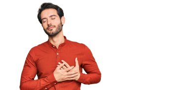 Gündelik kıyafetler giyen genç İspanyol adam elleri göğsünde, gözleri kapalı ve yüzünde minnet dolu bir jest ile gülümsüyor. sağlık kavramı. 