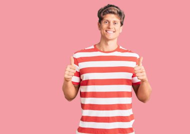 Gündelik kıyafet giyen yakışıklı bir adam. Başarı işareti yapıyor. Elleriyle olumlu jest yapıyor. Neşeli ifade ve kazanan jest. 