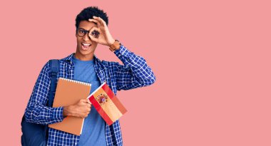 Afrika kökenli Amerikalı genç bir adam sırt çantası takıyor. Elinde İspanyol bayrağı var. Gülümsüyor. 