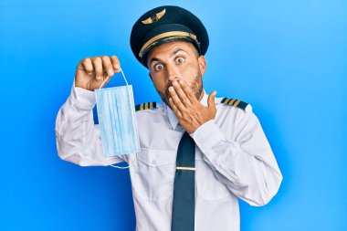 Sakallı, uçak pilotu üniforması giyen, güvenlik maskesi takan, ağzı ağızla kaplı, şok olmuş ve hata yapmaktan korkan yakışıklı bir adam. şaşırmış ifade 