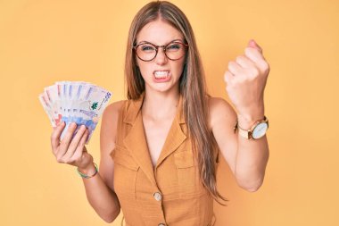 Kolombiya pezosu tutan genç sarışın kız öfkeyle bağırıyor, öfkeyle bağırıyor ve el kaldırıyor. 