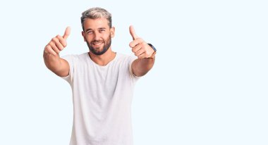 Genç, sarışın, sıradan tişörtler giyen, gülümseyen, elleri ve parmakları gülen yüzlü genç bir adam. yaratıcılık ve fotoğrafçılık kavramı. 