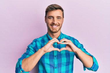 Gündelik kıyafetler giyen yakışıklı beyaz adam. Sevgiyle gülümseyen, kalp sembolü ve elleri ile şekil veren. romantik kavram. 