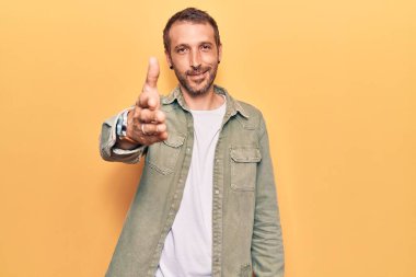 Gündelik kıyafetler giyen genç yakışıklı adam dostça bir selamlama ve hoş geldin hediyesi olarak el sıkışmayı sunuyor. başarılı iş. 