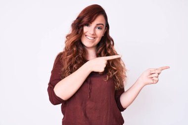 Genç, güzel bir kadın, günlük kıyafetler giyip gülümsüyor ve kameraya bakıyor. İki eliyle ve parmaklarıyla kenarı işaret ediyor.. 