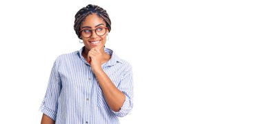 Saçları günlük kıyafet ve gözlük takan genç Afro-Amerikalı kadın kameraya kollarını kavuşturup gülümseyerek ve çenesini kaldırarak bakıyor. Olumlu düşünmek. 