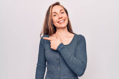 Genç, güzel, sarışın bir kadın izole edilmiş beyaz arka planda duruyor. Gülümsüyor, elleri ve parmakları yana doğru uzanıyor. 