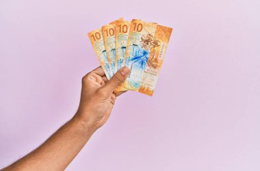 İspanyol el, izole edilmiş pembe arka planda 10 İsviçre frangı banknot tutuyor..