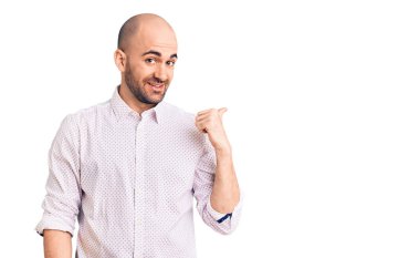 Zarif bir gömlek giyen, gülümseyen, gülümseyen, gülümseyen ve baş parmağıyla yan tarafı gösteren genç yakışıklı bir adam.. 