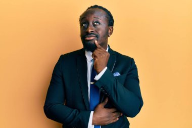 Yakışıklı, takım elbiseli ve kravatlı genç bir adam şüpheye odaklanmış, parmakları çenesinde ve yukarı bakıyor. 