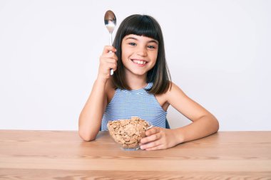 Bangır bangır oturmuş mısır gevreği yiyor. Olumlu ve mutlu görünüyor. Kendine güvenen bir gülümsemeyle dişlerini gösteriyor. 