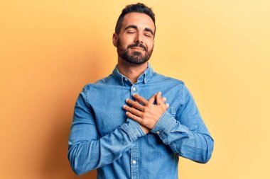 Gündelik kıyafetler giyen genç İspanyol adam elleri göğsünde, gözleri kapalı ve yüzünde minnet dolu bir jest ile gülümsüyor. sağlık kavramı. 