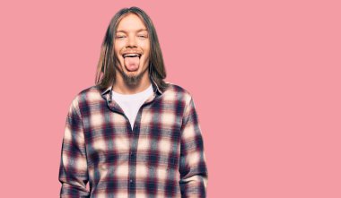 Uzun saçlı, hippi tişörtü giyen yakışıklı beyaz adam komik bir ifadeyle dilini dışarı çıkarıyor. duygu kavramı. 