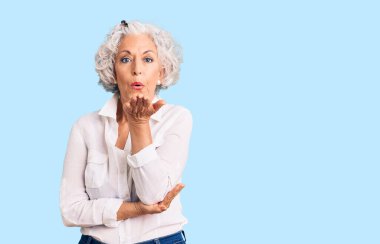 Kıdemli, gri saçlı, sıradan kıyafetler giyen, kameraya bakıp havada el ele öpüşen, güzel ve seksi bir kadın. aşk ifadesi. 