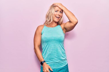 Pembe arka planda spor giysiler giyen orta yaşlı, beyaz bir kadın. Yanlışlıkla el ele tutuşarak şaşırmış. Hatayı hatırla. Unuttum, kötü hafıza kavramı. 