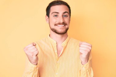 Gündelik giysiler giyen genç yakışıklı adam şaşkınlık ve şaşkınlık içinde kollarını kaldırarak ve gözlerini açarak başarıyı kutluyor. Kazanan konsept. 