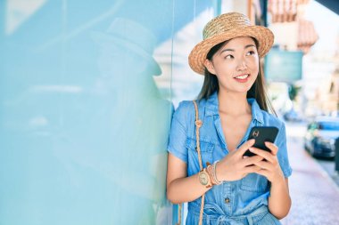 Genç Çinli turist şehrin duvarına dayanmış akıllı telefon kullanıyor..