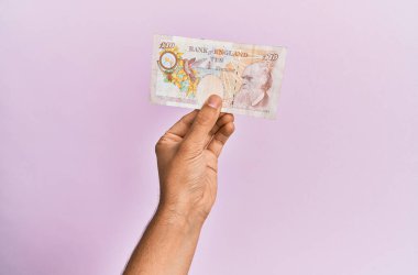 İspanyol eli, pembe arka planda 10 poundluk banknot tutuyor..