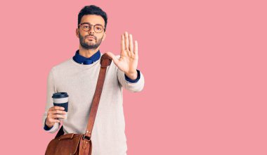 Deri çanta giyen ve kahve içen genç yakışıklı İspanyol adam dur işareti yapıyor. Ciddi ve kendinden emin bir ifade, savunma jesti. 