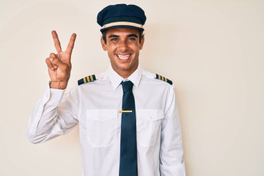 Uçak pilotu üniforması giyen genç İspanyol adam kameraya bakıp zafer işareti yapıyor. İki numara.. 