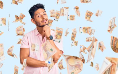 Yakışıklı Latin Amerikalı rahat bir yaz tişörtü giymiş kollarını kavuşturup kameraya gülümseyen ve çenesini kaldırmış kendine güvenen genç adam. Olumlu düşünmek.