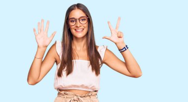 Genç İspanyol kadın, günlük kıyafetler ve gözlük takıyor. Sekiz numaralı parmaklarıyla işaret ediyor ve gülümsüyor. Kendinden emin ve mutlu.. 