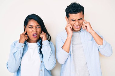 Gürültülü müzik sesi için kulaklarını parmaklarıyla kapatan gündelik kıyafetler giyen genç ve güzel Latin bir çift. sağır kavramı. 