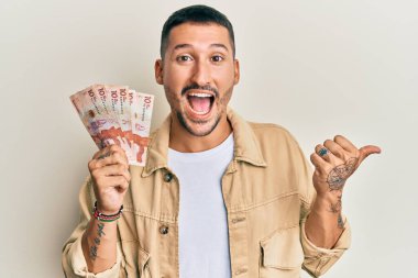 Elinde 10 Kolombiya pezosu olan yakışıklı bir adam baş parmağını kaldırmış, ağzı açık gülümsüyor. 