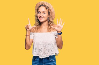 Kafkasyalı güzel bir kadın yaz şapkası takıyor ve yedi numaralı parmaklarıyla işaret ediyor. Kendinden emin ve mutlu bir şekilde gülümsüyor.. 