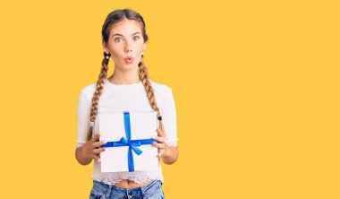 Sarışın, güzel, beyaz bir kadın elinde hediyesini tutuyor. Korkmuş ve ağzı açık, şaşırmış, inançsız bir yüz ifadesi var. 