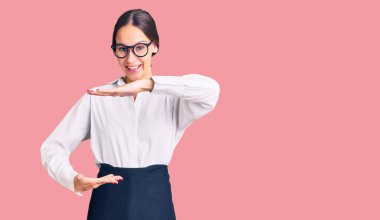 Güzel esmer, profesyonel garson önlüğü giyen, elleri büyük ve büyük beden işareti olan genç bir kadın. Ölçü sembolü. Kameraya bakıp gülümsüyor. ölçüm kavramı. 