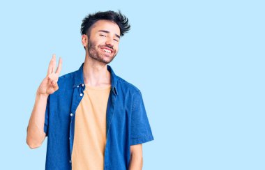 Gündelik kıyafetler giyen genç İspanyol adam üç numarayı gösterip işaret ederken kendinden emin ve mutlu gülümsüyor.. 