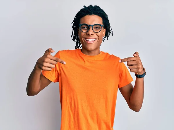 若いアフリカ系アメリカ人の男性は 笑顔で自信を持って見えるカジュアルな服や眼鏡を身に着けて 誇りに思って幸せな指で自分自身を指して — ストック写真