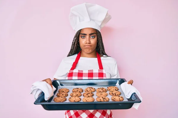 Молода Афроамериканська Жінка Плечима Формі Пекаря Тримає Домашнє Печиво Скептично — стокове фото