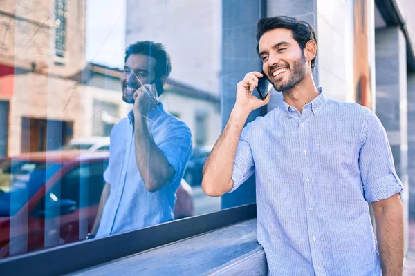 若いヒスパニック系の男笑顔幸せな話でスマートフォンの壁にもたれて — ストック写真