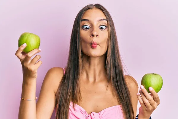 年轻的惊慌失措的女人拿着绿色的苹果 用嘴和眼神做鱼脸 疯狂而滑稽 — 图库照片