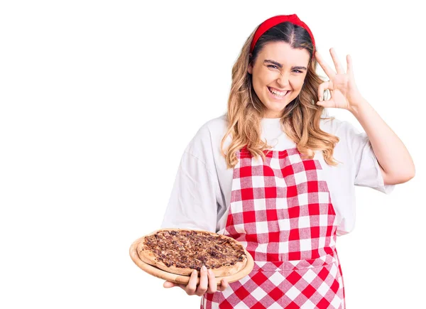 Jovem Mulher Caucasiana Vestindo Avental Segurando Pizza Fazendo Sinal Com — Fotografia de Stock