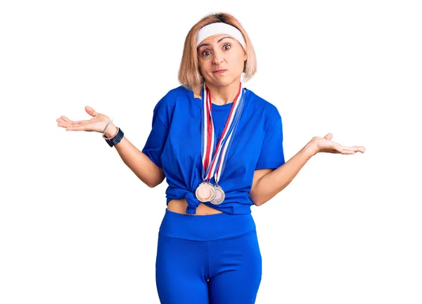 勝者のメダルを身に着けている若いブロンドの女性は 腕や手と無関心で混乱した表情を上げました 疑わしい概念 — ストック写真