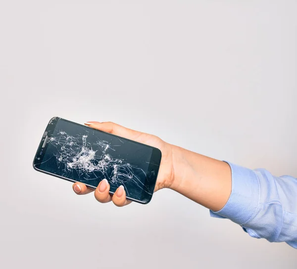 Hand of caucasian young woman holding broken smartphone showing craked screen over isolated white background