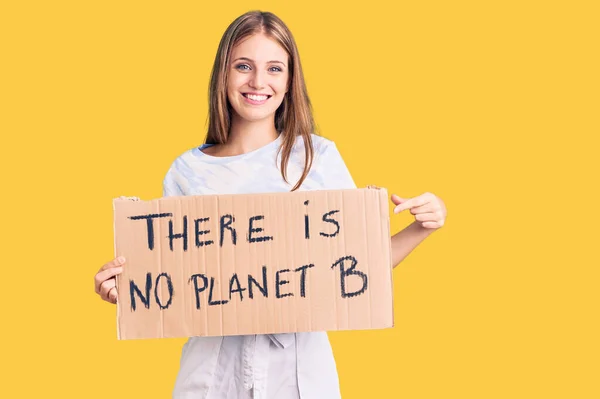 Young beautiful blonde woman holding there is no planet b banner smiling happy pointing with hand and finger