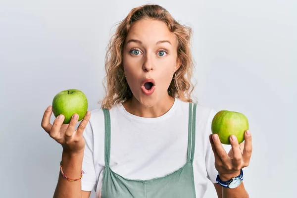 緑のリンゴを持っている美しい白人女性は恐れて 驚きと驚きの表情でショックを受けました 恐怖と興奮した顔 — ストック写真