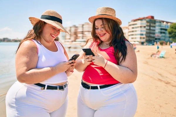 二つのプラスサイズ太りすぎ姉妹双子女性幸せなですビーチで夏休みとともにスマートフォン — ストック写真