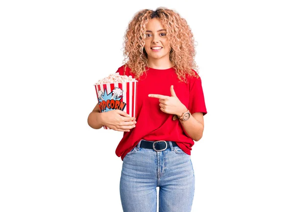 Mladá Blondýnka Kudrnatými Vlasy Jíst Popcorn Úsměvem Šťastný Ukazující Rukou — Stock fotografie