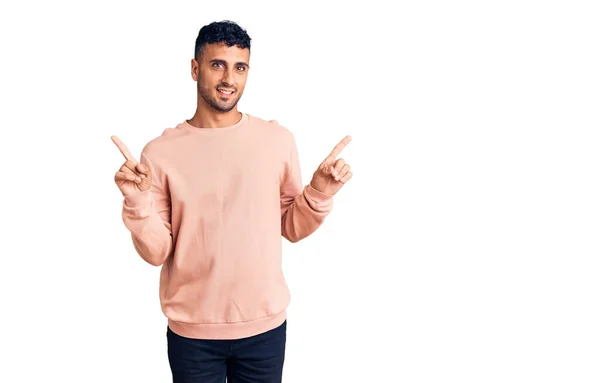 若いヒスパニック系の男性が別の方向に指で自信を持って指して笑顔カジュアルな服を着て 広告のコピースペース — ストック写真