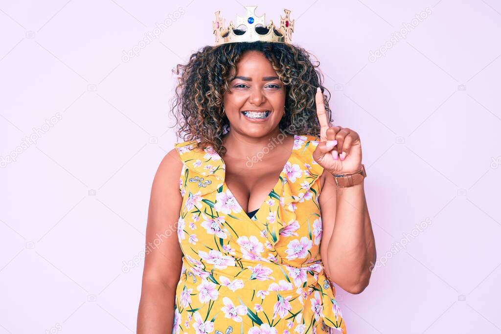 Young african american plus size woman wearing princess crown smiling with an idea or question pointing finger up with happy face, number one 